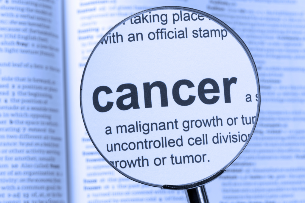 Magnifying glass highlighting the word “cancer” and its definition about uncontrolled cell growth in a dictionary.
